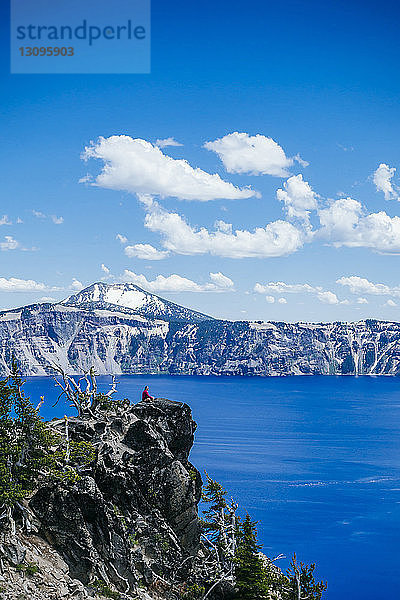 Mitteldistanzansicht eines auf Felsen sitzenden Wanderers im Crater Lake National Park