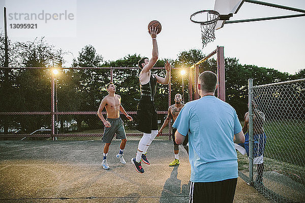 Freunde schauen einem Mann zu  der bei Sonnenuntergang beim Basketballtraining auf dem Platz eintaucht
