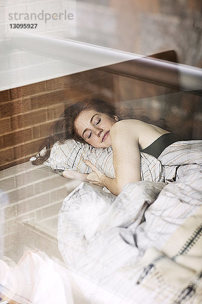 Lächelnde Frau  die zu Hause auf dem Bett schläft  durch Glas gesehen