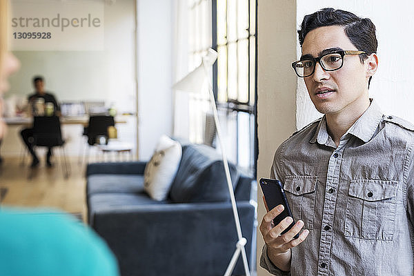 Geschäftsmann hält Mobiltelefon  während er mit seinem Amtskollegen diskutiert