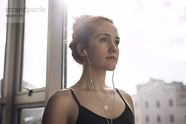 Niedriger Blickwinkel einer nachdenklichen Frau  die Musik hört  während sie zu Hause am Fenster steht