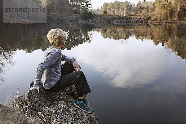 Junge sitzt auf einem Felsen am See
