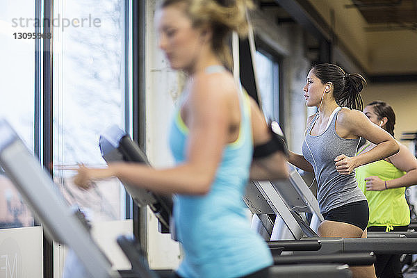 Frauen  die Musik hören  während sie im Fitnessstudio auf Laufbändern trainieren