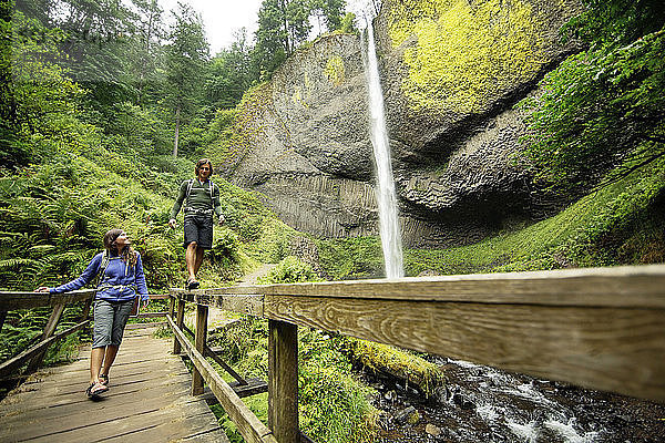 Paar zu Fuss auf Steg am Wasserfall im Wald