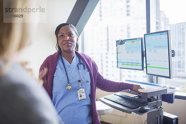 Ärztin  die den Patienten ansieht  während sie im Behandlungszimmer an den Desktop-Computern steht