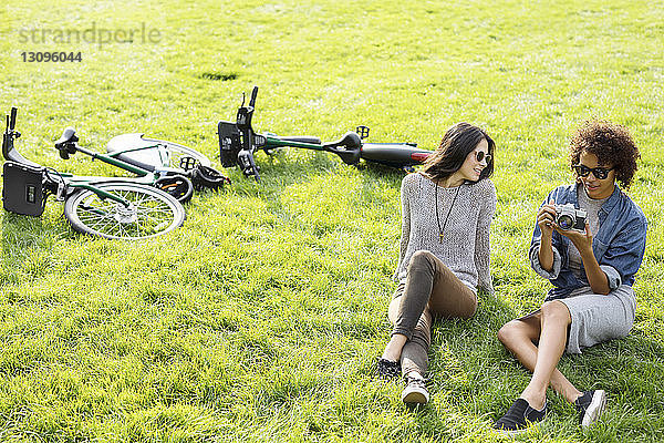Hochwinkelaufnahme von Freunden mit Kamera  die sich auf einem Grasfeld entspannen