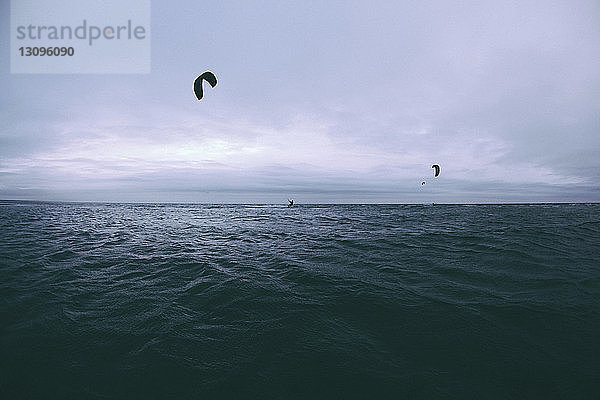 Menschen beim Kitesurfen über dem Meer gegen bewölkten Himmel