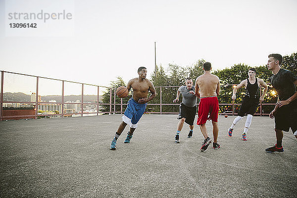 Männliche Freunde spielen Basketball vor Gericht gegen klaren Himmel