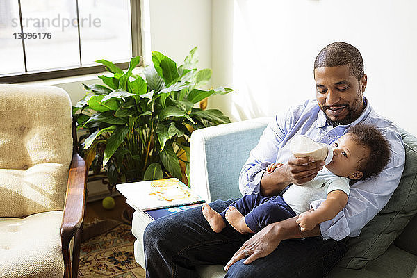 Hochwinkelaufnahme eines Vaters  der ein Baby mit Milch füttert  während er auf einem Sessel sitzt