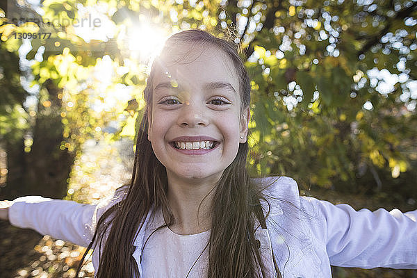 Nahaufnahme-Porträt eines lächelnden Mädchens mit ausgestreckten Armen im Park stehend