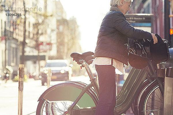 Seitenansicht der älteren Frau beim Entriegeln des Fahrrads vom Gepäckträger