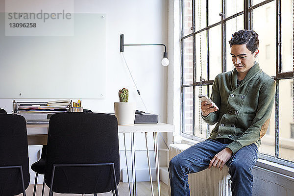 Geschäftsmann telefoniert  während er auf dem Fensterbrett am Schreibtisch im Büro steht