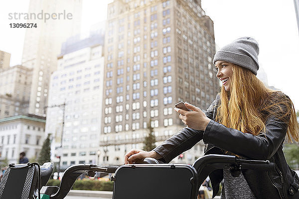 Glückliche Frau hält Handy in der Hand  während sie am Fahrradparkplatz steht