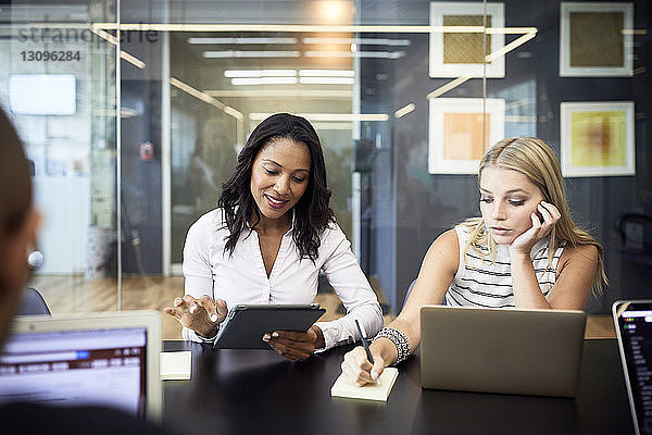 Geschäftsfrauen  die Technologien nutzen  während sie bei Besprechungen am Konferenztisch sitzen