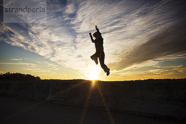 Silhouette eines Jungen  der bei Sonnenuntergang gegen den Himmel springt