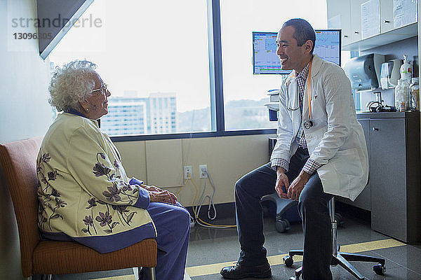 Lächelnder männlicher Arzt im Gespräch mit Patient auf der Krankenhausstation