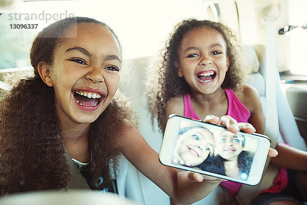 Glückliches Mädchen zeigt Foto in Smartphone  während es mit seiner Schwester unterwegs ist