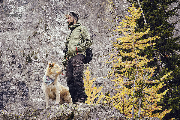 Niedrigwinkelansicht eines Mannes mit Hund  der im Winter auf einer Felsformation steht