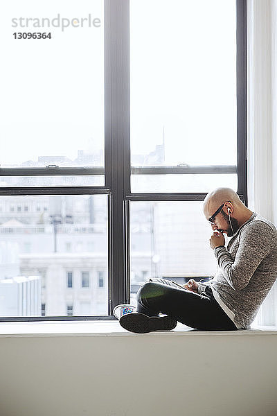 Seitenansicht eines Geschäftsmannes  der ein Smartphone benutzt  während er am Fenster sitzt