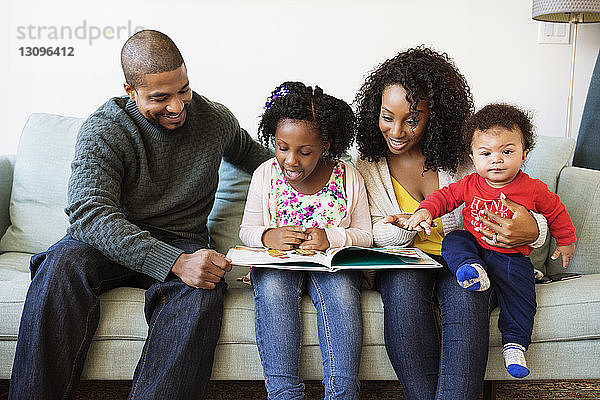 Glückliche Familie schaut ins Bilderbuch  während sie auf dem Sofa sitzt