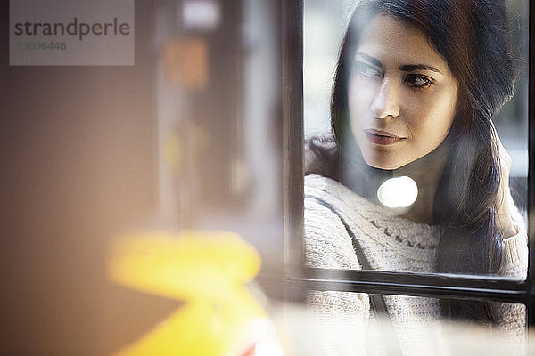 Nachdenkliche junge Frau durch Glaswand gesehen