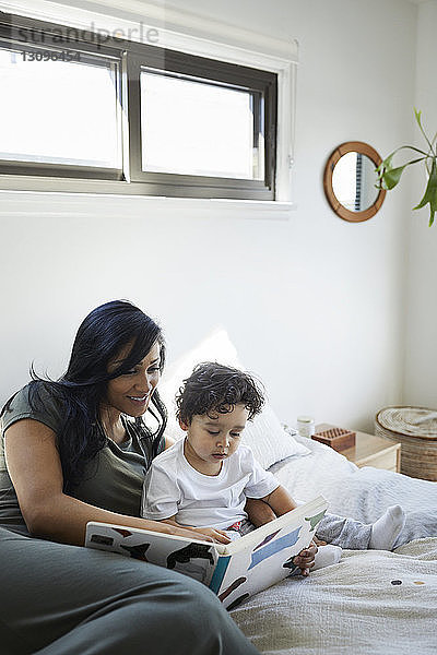 Mutter und Sohn schauen Bilderbuch an  während sie zu Hause im Bett liegen