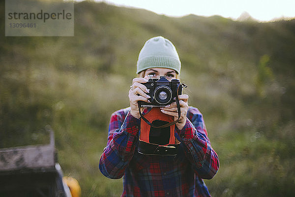 Junge Frau fotografiert mit der Kamera  während sie auf dem Feld steht