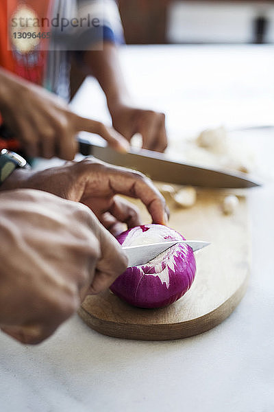 Ausgeschnittenes Bild eines Paares  das Zwiebel und Knoblauch in der Küche schneidet