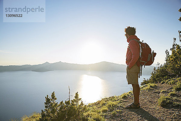 Wanderer mit Rucksack steht am sonnigen Tag auf einem Berg im Crater Lake National Park