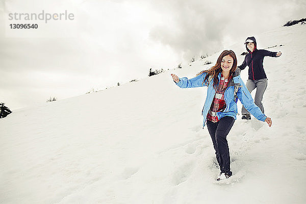 Fröhliche Freundinnen rennen auf schneebedecktem Berg gegen die Wolken