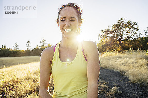 Frau lächelt  während sie am sonnigen Tag auf dem Feld gegen den klaren Himmel steht