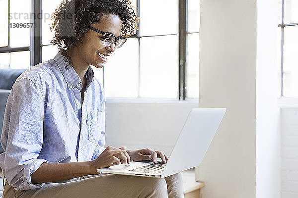 Glückliche Geschäftsfrau benutzt Laptop-Computer  während sie im Büro sitzt