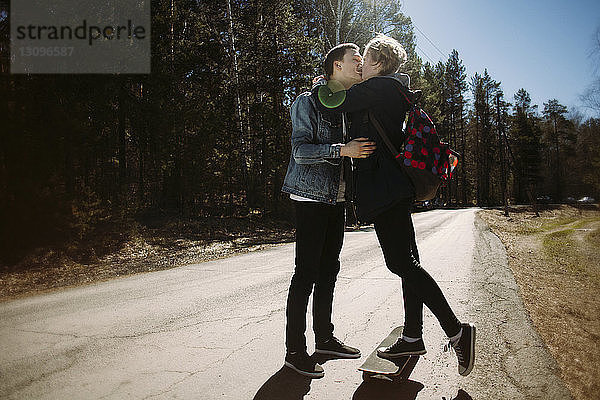 Romantisches Paar küsst sich an einem sonnigen Tag auf einer Straße im Wald