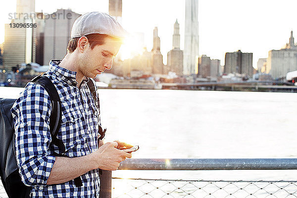 Mann benutzt Smartphone  während er an der Reling am East River steht