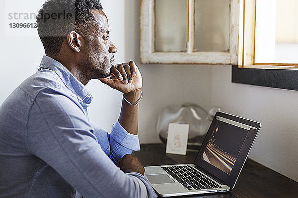 Nachdenklicher Mann schaut weg  während er zu Hause mit einem Laptop-Computer sitzt