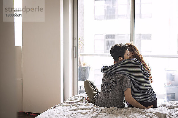 Romantische Lesben umarmen sich  während sie zu Hause auf dem Bett sitzen