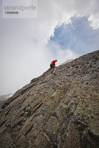 Tiefwinkelansicht eines entschlossenen Wanderers  der an Felsformationen vor bewölktem Himmel klettert