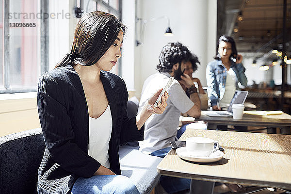 Geschäftsfrau nutzt Smartphone mit im Hintergrund arbeitenden Geschäftsleuten