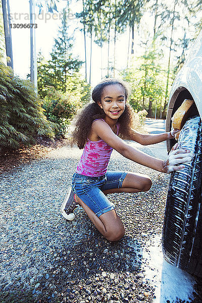 Porträt eines knienden Mädchens beim Autowaschen in der Einfahrt