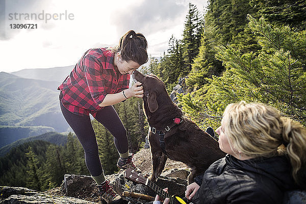 Frauen genießen mit Hund auf Bergfelsen gegen den Himmel