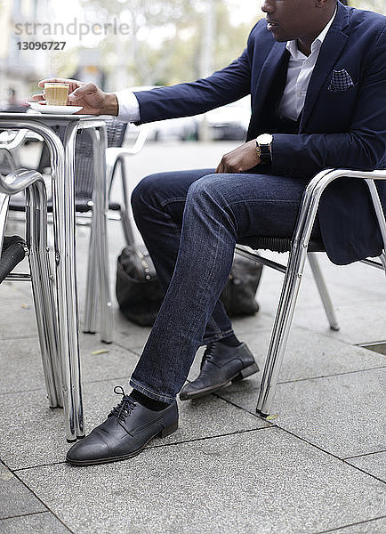 Niedriger Teil des Geschäftsmannes sitzt im Straßencafé