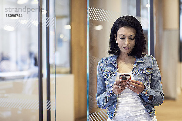Geschäftsfrau benutzt Smartphone  während sie sich im Büro an die Tür lehnt