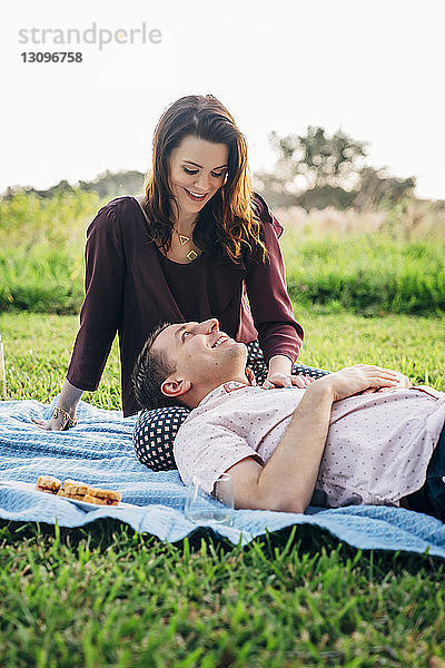 Lächelnder Ehemann entspannt sich auf dem Schoß der Frau vor klarem Himmel im Park