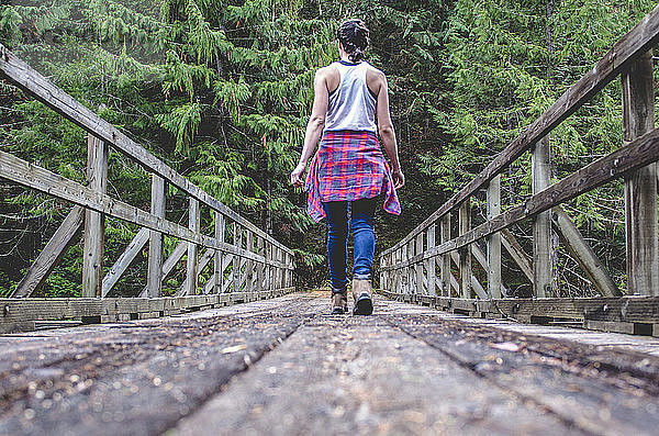 Rückansicht einer Frau  die auf einem Steg inmitten von Bäumen im Wald geht