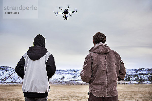 Rückansicht von Vater und Sohn  wie sie im Winter Drohne über das Feld fliegen
