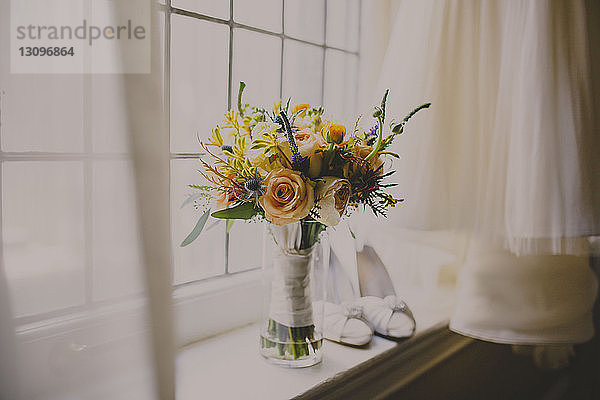 Blumenvase und Schuhe auf der Fensterbank beim Brautkleid