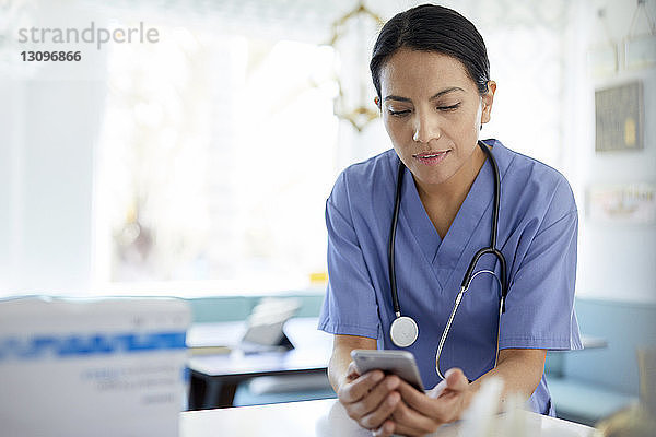 Ärztin mit Stethoskop  die während der Arbeit im Krankenhaus ein Smartphone benutzt