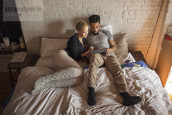 Draufsicht eines multiethnischen Paares mit Tablet-Computer am Bett