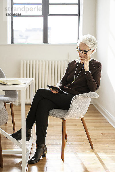 Ältere Geschäftsfrau benutzt digitales Tablet  während sie im Büro sitzt