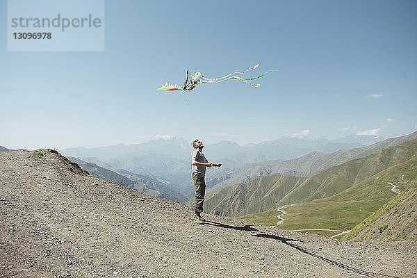 Wanderer lässt bei Sonnenschein Drachen gegen Berge und Himmel fliegen